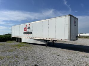 A large white trailer parked on top of a gravel road.