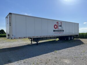 A large white trailer parked on top of a gravel road.