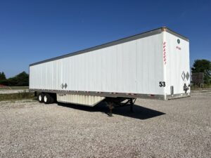 A white trailer parked in the middle of a gravel lot.