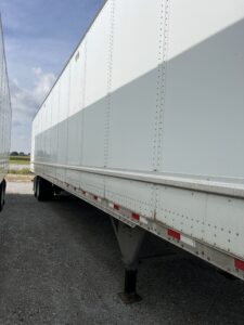 A white semi-trailer parked on a gravel surface.