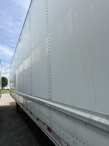Side view of a large white trailer against a partly cloudy sky.