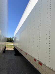 Two white semi-truck trailers parked closely side by side under a clear sky.