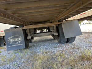 Underside view of a truck showing its axle and wheels on gravel.