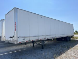 Empty white semi-trailer parked on gravel under clear sky.