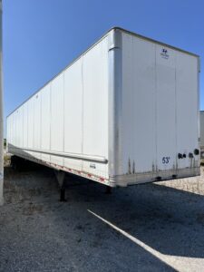 White semi-trailer parked on gravel with clear blue sky.