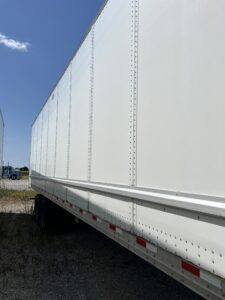 Side view of a large white trailer under a clear blue sky.